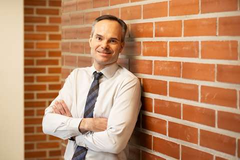 Kaupunginjohtaja Kai Mykkänen nojaa tiiliseinään ja hymyilee, puolivartalokuva.