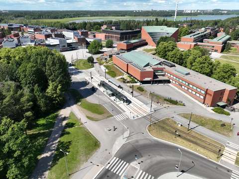 Red brick buildings, roads, a light rail, tram tracks, trees, and the sea in the background.
