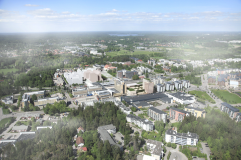 Ilmakuva, jossa näkyy kerrostaloja, puita, teitä ja junaraiteet. Kuvaan on lisätty hahmotelmia tulevista rakennuksista.