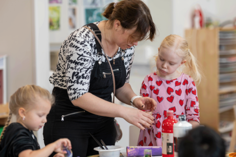 Kaksi päiväkodin lasta ja opettaja askartelevat.