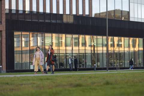 Suuren rakennuksen edessä kävelee kaksi ihmistä.