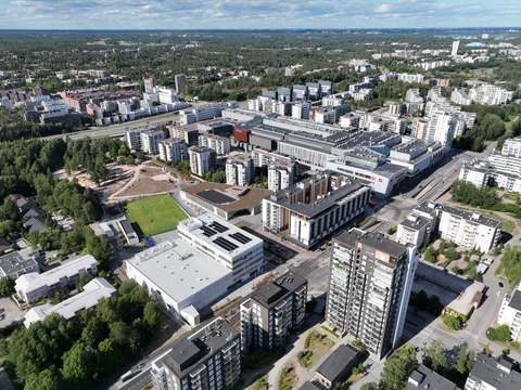 Ilmakuva, jossa näkyy eri korkuisia rakennuksia, vihreitä puita ja liikenneväyliä.