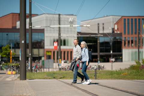 Kaksi kävelijää kadulla. Taustalla näkyy iso rakennus, jossa on myös metroasema.