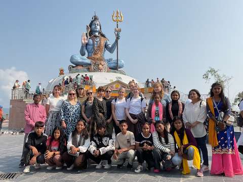 En grupp människor i olika åldrar i Nepal framför en staty.