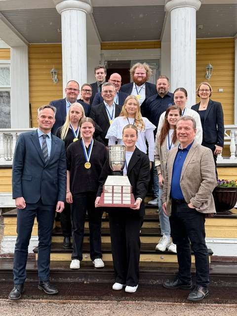 Kuvassa ryhmä naisia ja miehiä poseeraa kartanon portailla. Eturivissä olevalla naisella on iso pokaali sylissään.