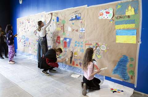 Ryhmä nuoria piirtää seinälle kiinnitetyille papereille värikkäitä kuvia.