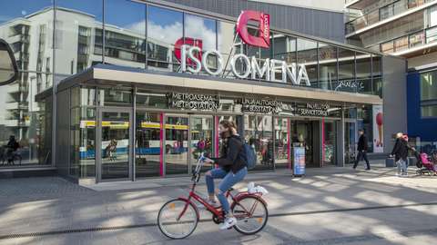 Kauppakeskuksen edessä olevaa katua polkee nainen pyörällä.