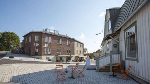 Valokuvassa aukio, jonka reunoilla vanha tiilirakennus ja puurakennus sekä kahvilapöytiä ja tuoleja.