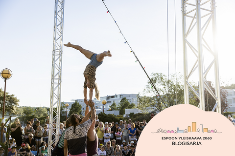 Voimistelunäytöksessä nainen seisoo käsillään häntä tukevien miesten käsien päällä. Taustalla kerrostaloja, puita ja esitystä seuraava yleisö.