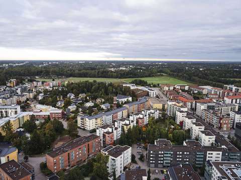 Ilmakuva Espoon Leppävaarasta: Yleisnäkymä tiiviisti rakennetusta kaupunkialueesta, jossa erottuvat asuinrakennukset, ostoskeskukset ja viheralueet. Valoisa päivä.