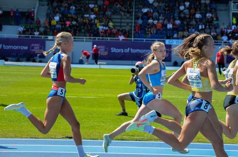 Naiset juoksevat kilpaa urheilukentällä. Taustalla katsomo, jossa on yleisöä.