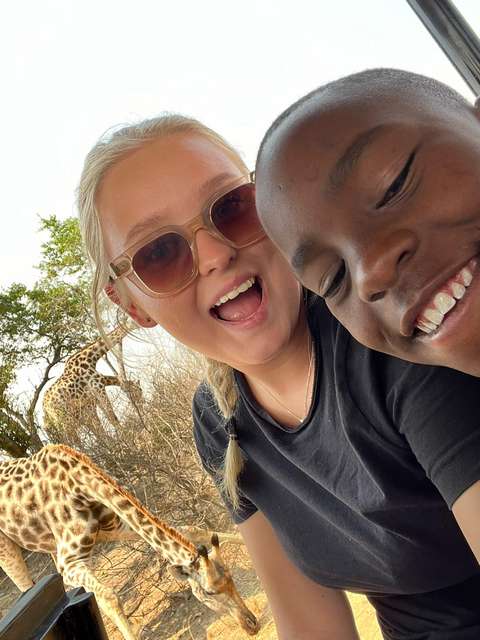 Kaksi hymyilevää nuorta ja kirahvi.