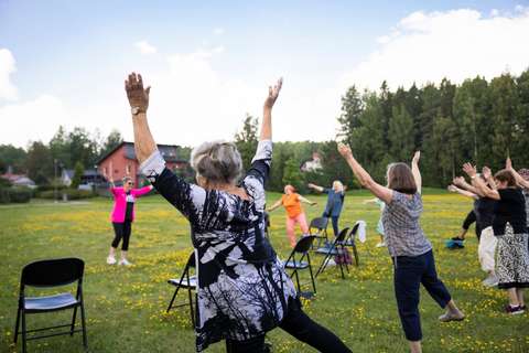 Several elderly people exercising outside on the green lawn under the guidance of an instructor. 