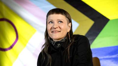 Hymyilevä henkilö Pride-lipun edessä. 