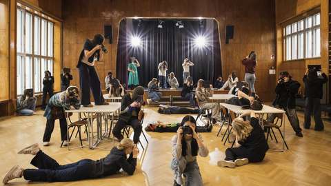 Flera elever i skolans idrottshall har intagit olika positioner och fotograferar.