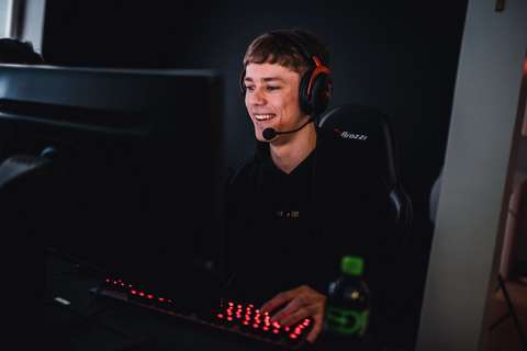 Nuori henkilö hymyilee ja pelaa tietokoneella kuulokkeet päässään.