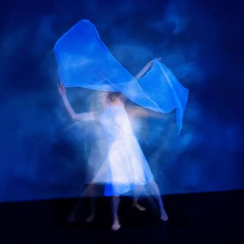 Epätarkka kuva liikkuvasta tanssijasta, jolla heiluttaa käsissään kangasta.