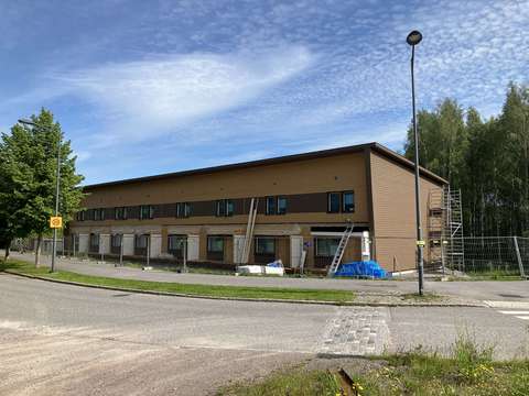 Kuvassa näkyy aidattu alue, jonka sisällä on rakenteilla oleva rivitalo. Kuvan etualalla autotie ja kevyen liikenteen väylä.