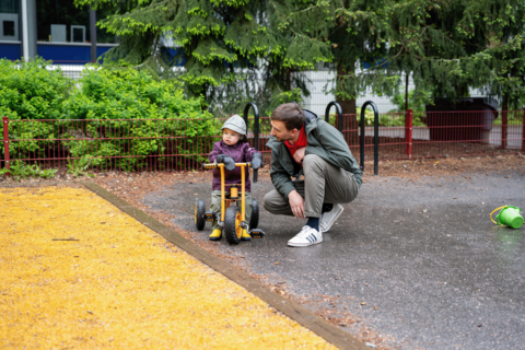 Lapsi harjoittelee asukaspuistossa polkupyörällä ajoa ja isä tukee vieressä.