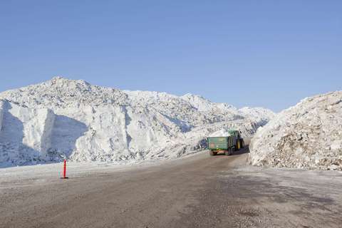 Photograph of a tractor carrying a snow load in the snow storage area between tall piles of snow.