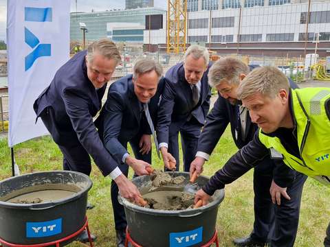 Viisi miestä muurauslastat käsissään kumartuneena laastiastian ääreen.