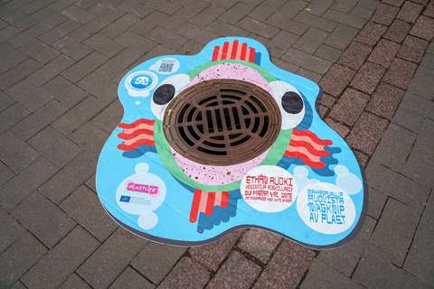 Den färggranna dekalen med en fisk är monterad runt brunnslocket med galler. Dekalens text: Magknip av plast.