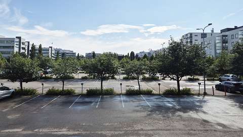 Etualalla suuri pysäköintikenttä, takana näkyy toimistokerrostaloja.