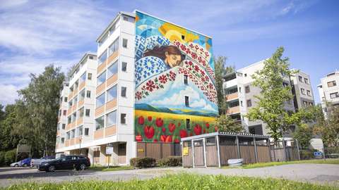 Kerrostalon seinässä on seinämaalaus, jossa henkilö nukkuu kirjailluiden liinavaatteiden keskellä. Seinämaalauksen alalaidassa on viljapelto, jossa kasvaa myös punaisia kukkia.