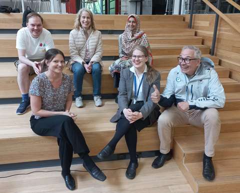 Kuusi hymyilevää aikuista henkilöä istuu puisilla portailla. 