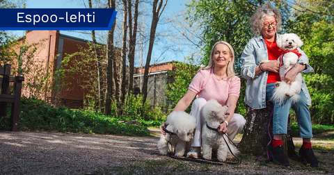 Sari Kaunisto on kyykistyneenä ja hänen edessään on kaksi koiraa, Meiju Kanttu istuu tuolilla ja pitää sylissään pientä koiraa. 