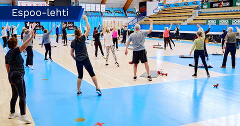 Seniors in a group exercise class in a gym hall with their backs to the camera.