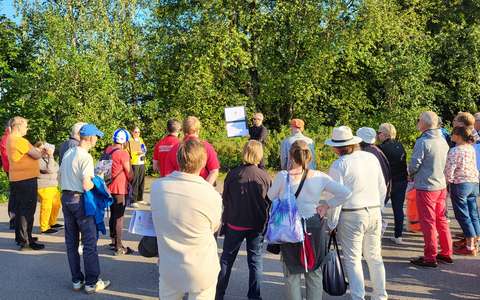 Ihmisiä ulkona kokoontuneena katsomaan paperilta suunnitelmakuvia.