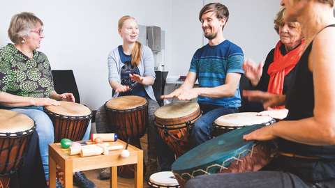 Ryhmä ihmisiä soittaa sylissä pidettäviä rumpuja yhdessä.