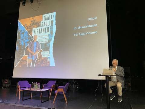 Luennoitsija seisoo auditorion lavalla ja puhuu mikrofoniin.