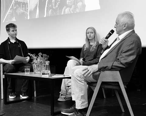 Kolme henkilöä keskustelee auditorion lavalla. 