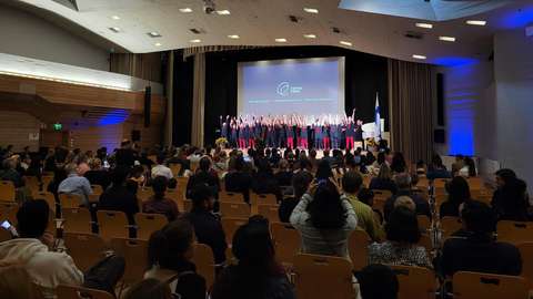 People sit in the hall and watch the performers standing on stage.
