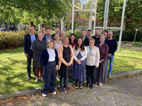 Valtuuston neuvottelutoimikunta seisoo ryhmäkuvassa ulkona viheralueella aurinkoisena päivänä.