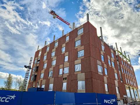 rakenteilla olevan rakennuksen julkisivu alaviistosta, edustalla näkyy rakennusliikkeen kyltti