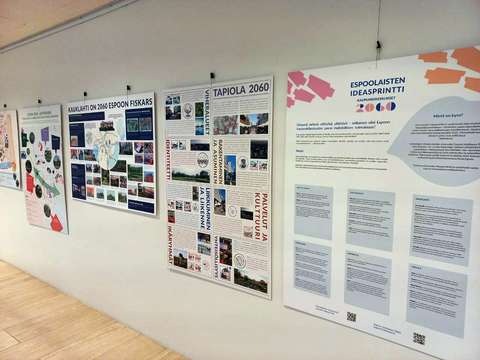 Suuria ja värikkäitä, tekstiä sisältäviä tauluja roikkuu ripustettuna valkoiselle seinälle.