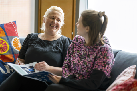 Två personer som arbetar inom småbarnspedagogiken sitter i soffan och samtalar om ett häfte som de har i famnen.