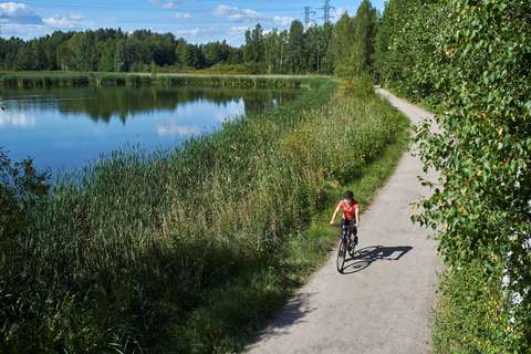 A cyclist on a sandy road by a pond with a forest in the background.