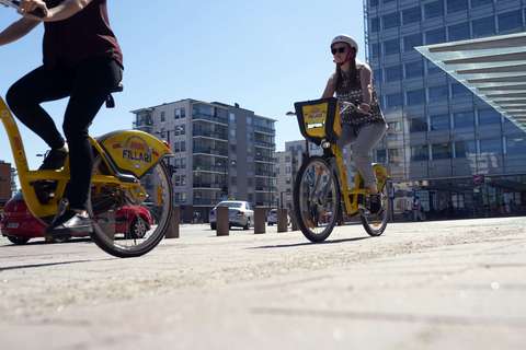 Pyöräileviä henkilöitä. Takana rakennuksia.