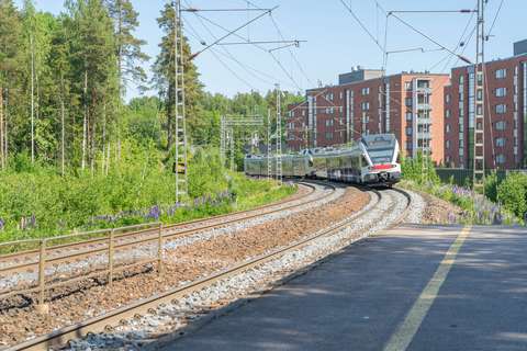 A train arriving at Koivuhovi railway station, with trees and apartment buildings in the background.