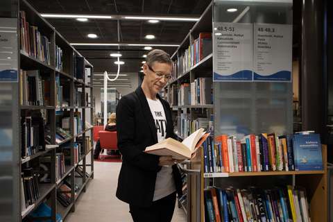 Ritva Nyberg selaa kirjaa hyllyjen edessä.
