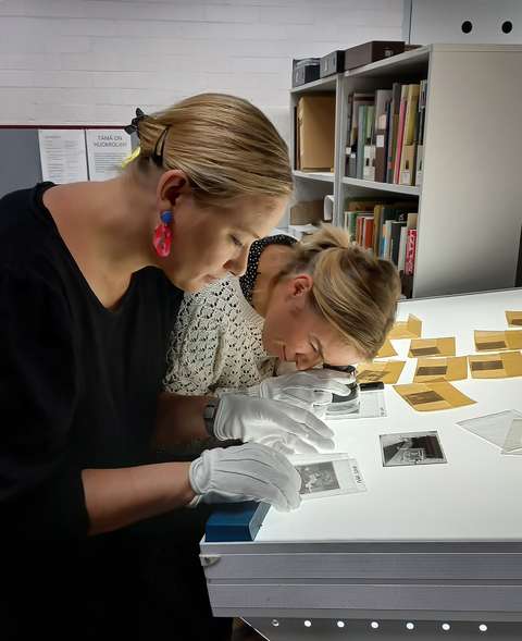 Two people bent over a glass table looking at photographic negatives.