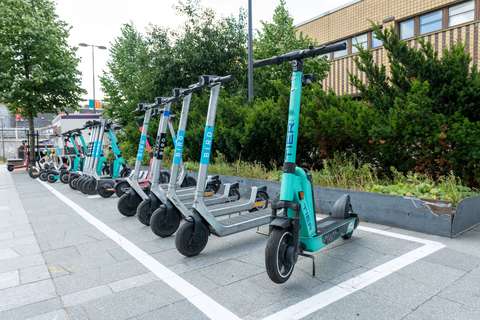 Elsparkcyklar i olika färger parkerade framför en kontorsbyggnad.