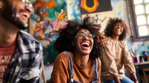 Kolme ihmistä istumassa ja nauramassa värikkään taustan edessä.