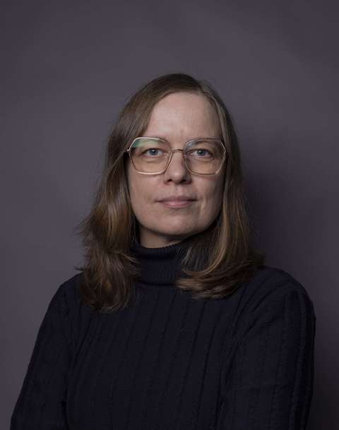  Potrettikuva naisesta tummassa puserossa tummaa taustaa vastaan.