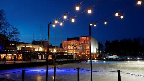 Edessä pimeässä valaistu jääkenttä ja matala rakennus. Takana Espoon kulttuurikeskus, joka on valaistu oranssilla värillä.