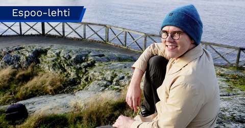 Oskar Rönnberg sitter på en klippa vid stranden och ser leende mot kameran. I bakgrunden syns räcket på en gångbro och havet.